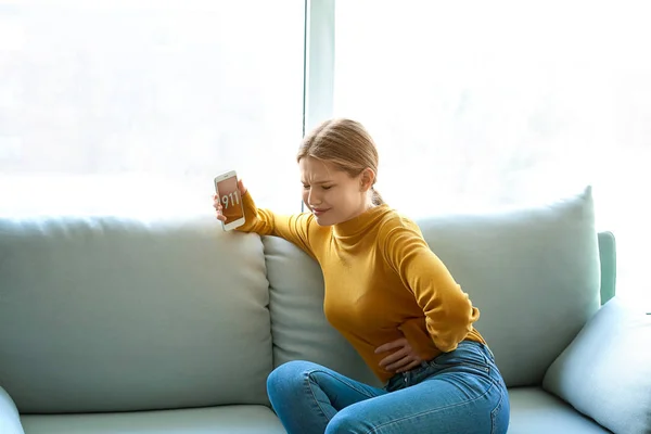 Mladá žena volá sanitku, zatímco trpí bolestí břicha doma — Stock fotografie