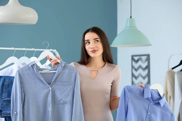 Jeune femme réfléchie choisissant des vêtements dans le vestiaire — Photo