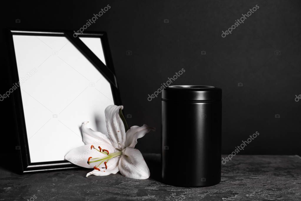 Mortuary urn with lily flower and frame on table against dark background