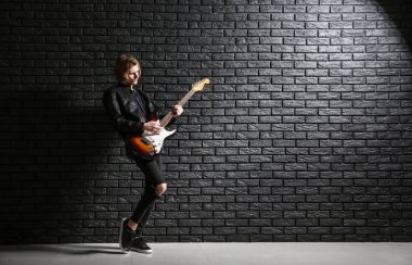 Yakışıklı genç adam koyu tuğla duvara karşı gitar çalıyor