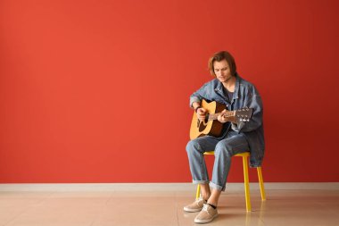 Yakışıklı genç adam renk duvara yakın gitar çalıyor