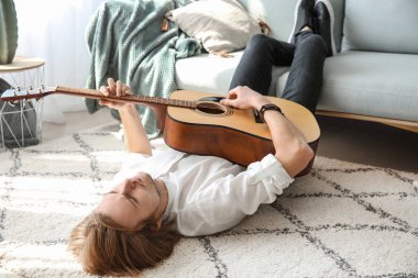 yakışıklı genç adam evde gitar çalıyor.
