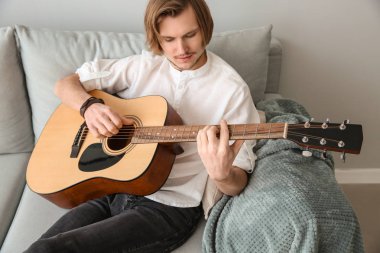 yakışıklı genç adam evde gitar çalıyor.