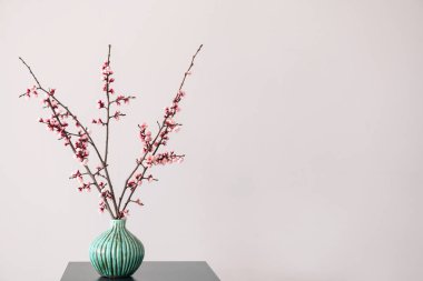 Masanın üzerinde çiçek açan güzel dalları olan bir vazo.