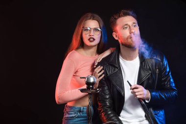 Genç çift karanlık arka planda nargile içiyor.