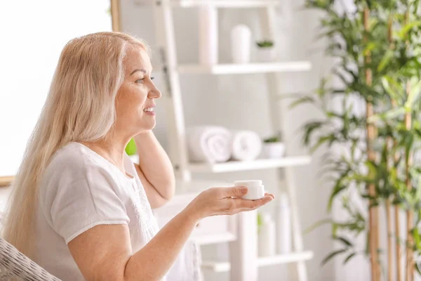 Mature woman applying facial cream at home — Stock Photo, Image