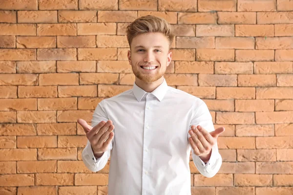 Schöner junger Mann lädt Betrachter vor gemauertem Hintergrund ein — Stockfoto