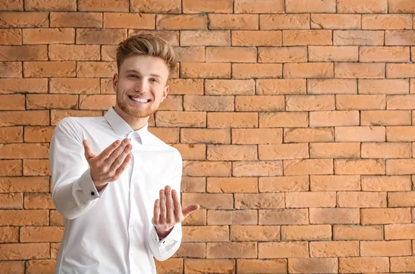 Schöner junger Mann lädt Betrachter vor gemauertem Hintergrund ein — Stockfoto