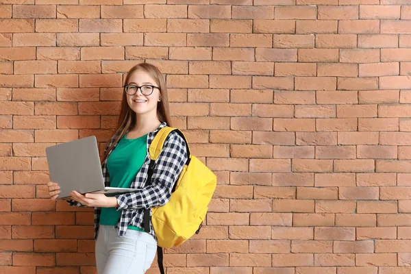 Cute teenage girl with laptop near brick wall — Stock Photo, Image