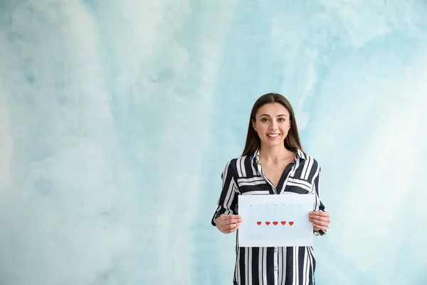 Woman holding calendar with marked days of menstruation on color background — Stock Photo, Image