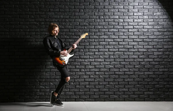 Guapo joven tocando la guitarra contra la pared de ladrillo oscuro — Foto de Stock