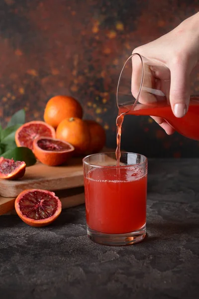 Mulher derramando suco de laranja de sangue fresco de jarro em vidro na mesa — Fotografia de Stock