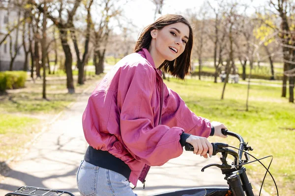 Beautiful young woman with bicycle in park on spring day — Stock Photo, Image
