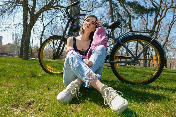 Beautiful young woman with bicycle in park on spring day — Stock Photo, Image