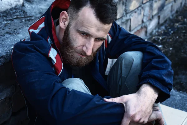 Arme dakloze man zitten in de buurt van de muur buitenshuis — Stockfoto