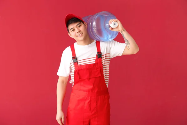 Asian delivery courier with bottle of water on color background — Stock Photo, Image