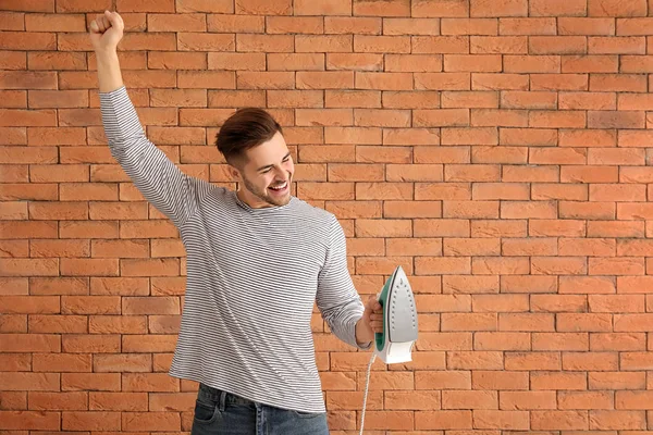 Happy young man with iron on brick background — Stock Photo, Image