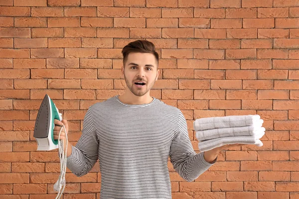 Stressed man with iron and towels on brick background — Stock Photo, Image