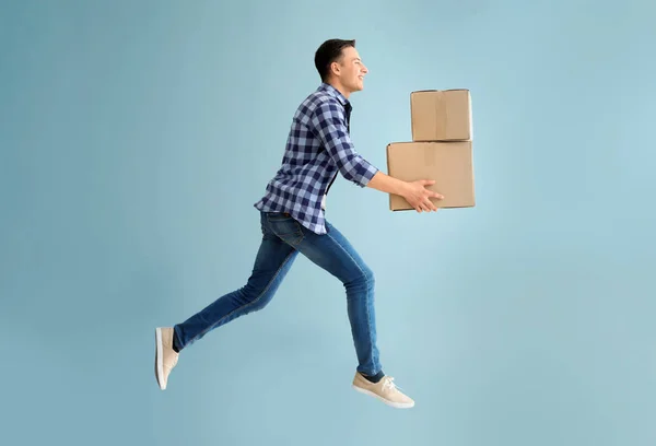 Jumping young man with boxes on grey background — Stock Photo, Image