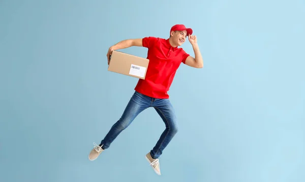 Jumping young male courier with box on grey background — Stock Photo, Image