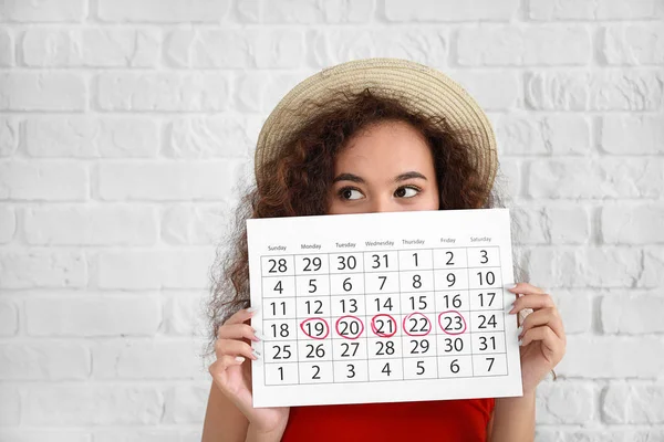 Афроамериканка проводит календарь с отмеченными днями менструации на белом фоне — стоковое фото