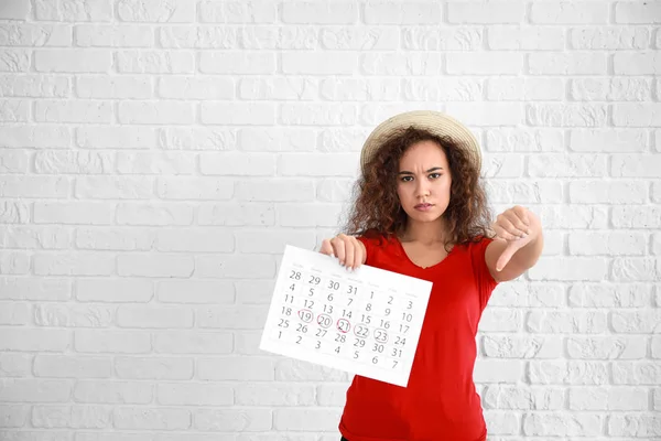 Афро-американка держит календарь с отмеченными днями менструации и показывает большой палец вниз на белом фоне — стоковое фото