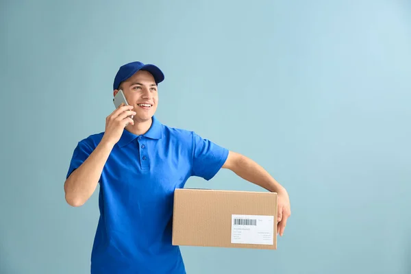Delivery man with box talking by phone on color background