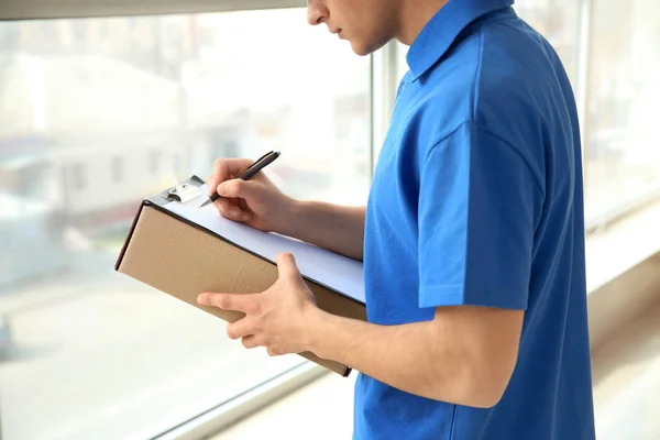 Delivery man with box and clipboard indoors — Stock Photo, Image