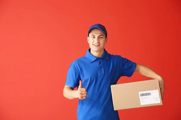 Entrega hombre con caja que muestra el pulgar hacia arriba en el fondo de color — Foto de Stock