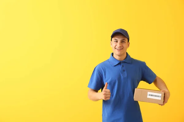 Delivery man with box showing thumb-up on color background — Stock Photo, Image