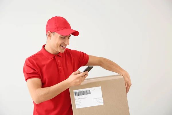Delivery man with box and mobile phone on light background — Stock Photo, Image