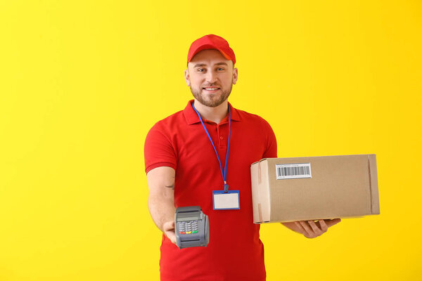 Handsome delivery man with parcel and payment terminal on color background