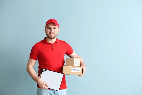 Schöner Zusteller mit Schachteln und Klemmbrett auf farbigem Hintergrund — Stockfoto