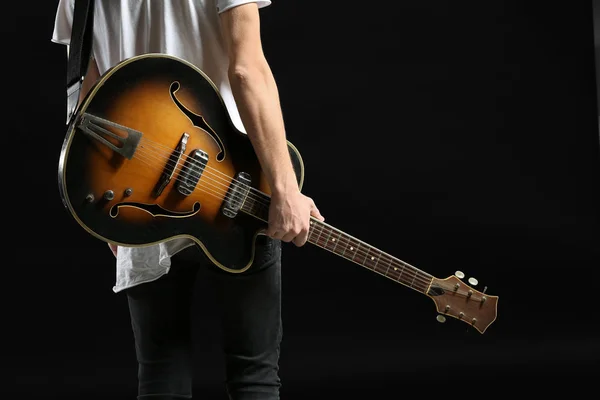 Bello giovane uomo con chitarra su sfondo scuro — Foto Stock