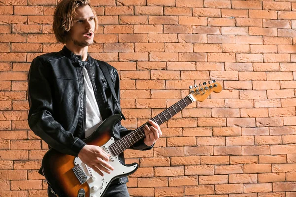 Handsome young man playing guitar against brick wall — Stock Photo, Image