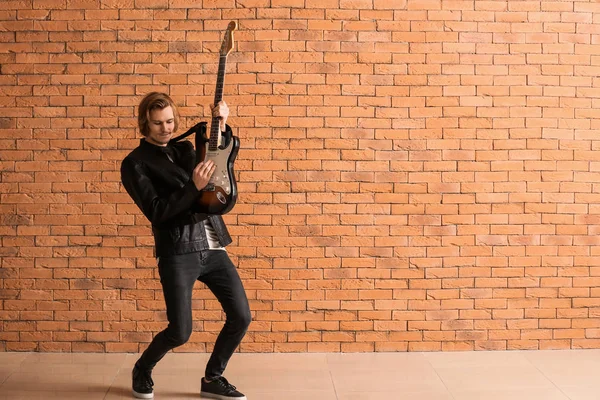 Bello giovane che suona la chitarra contro il muro di mattoni — Foto Stock