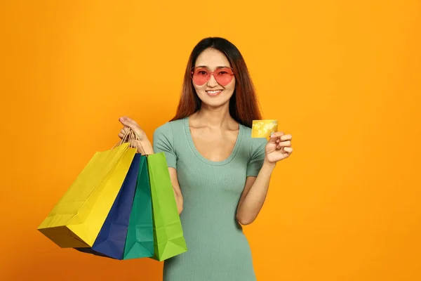 Asijská žena s nákupními taškami a kreditní kartou na barevném pozadí — Stock fotografie