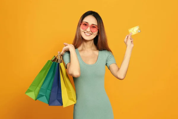 Aziatische vrouw met boodschappentassen en creditcard op kleur achtergrond — Stockfoto