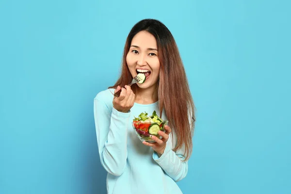 Aziatische vrouw met groente salade op kleur achtergrond — Stockfoto