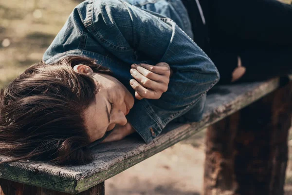 Poor homeless woman lying on bench outdoors