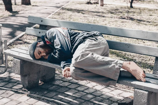 Pobre sem-teto deitado no banco ao ar livre — Fotografia de Stock