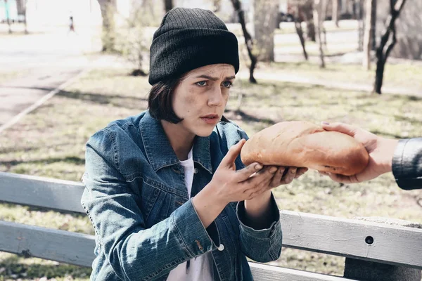 Прохожий дает хлеб бедной бездомной женщине на улице — стоковое фото