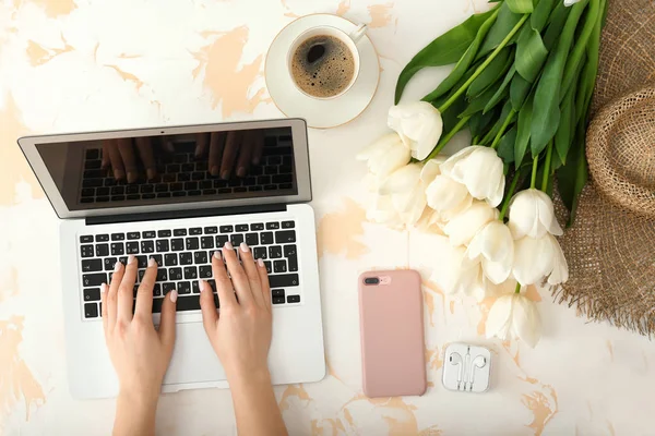Woman working on laptop at table with beautiful tulip flowers — Stock Photo, Image