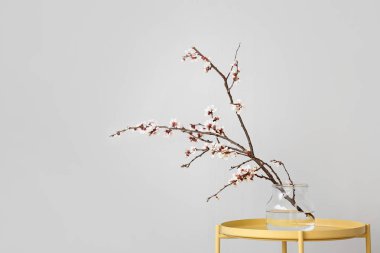 Masanın üzerinde çiçek açan güzel dalları olan bir vazo.