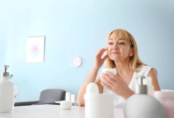 Mulher madura aplicando creme facial em casa — Fotografia de Stock