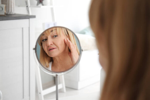 Mature woman looking in mirror at home