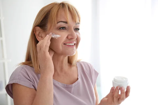 Mulher madura aplicando creme facial em casa — Fotografia de Stock