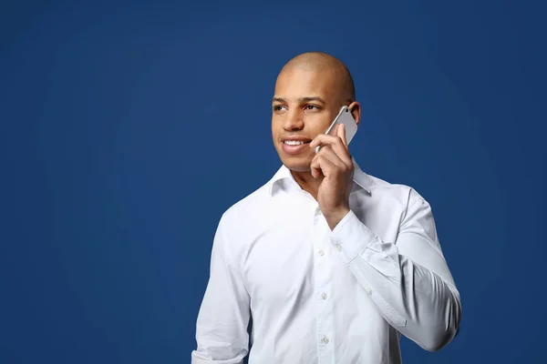 Handsome African-American man talking by phone on color background — Stock Photo, Image