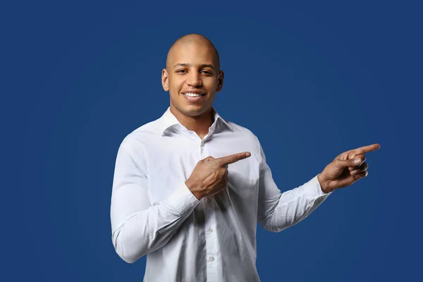 Handsome African-American man pointing at something on color background — Stock Photo, Image