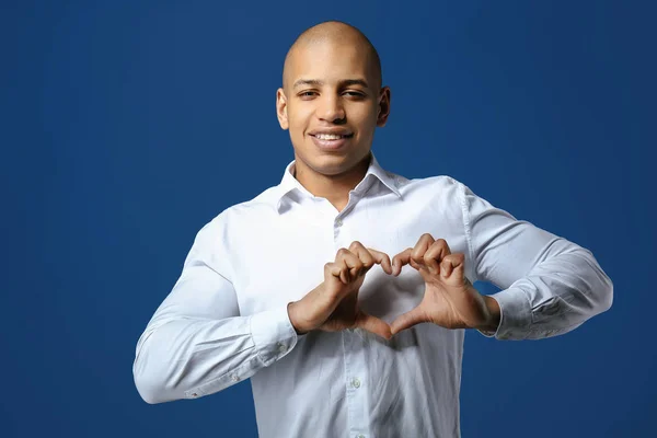 Handsome African-American man making heart with his hands on color background — Stock Photo, Image